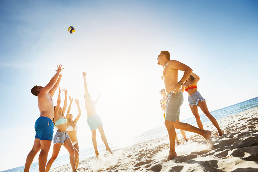 Група приятели, играещи игра с топка на плажа на фона на залез слънце